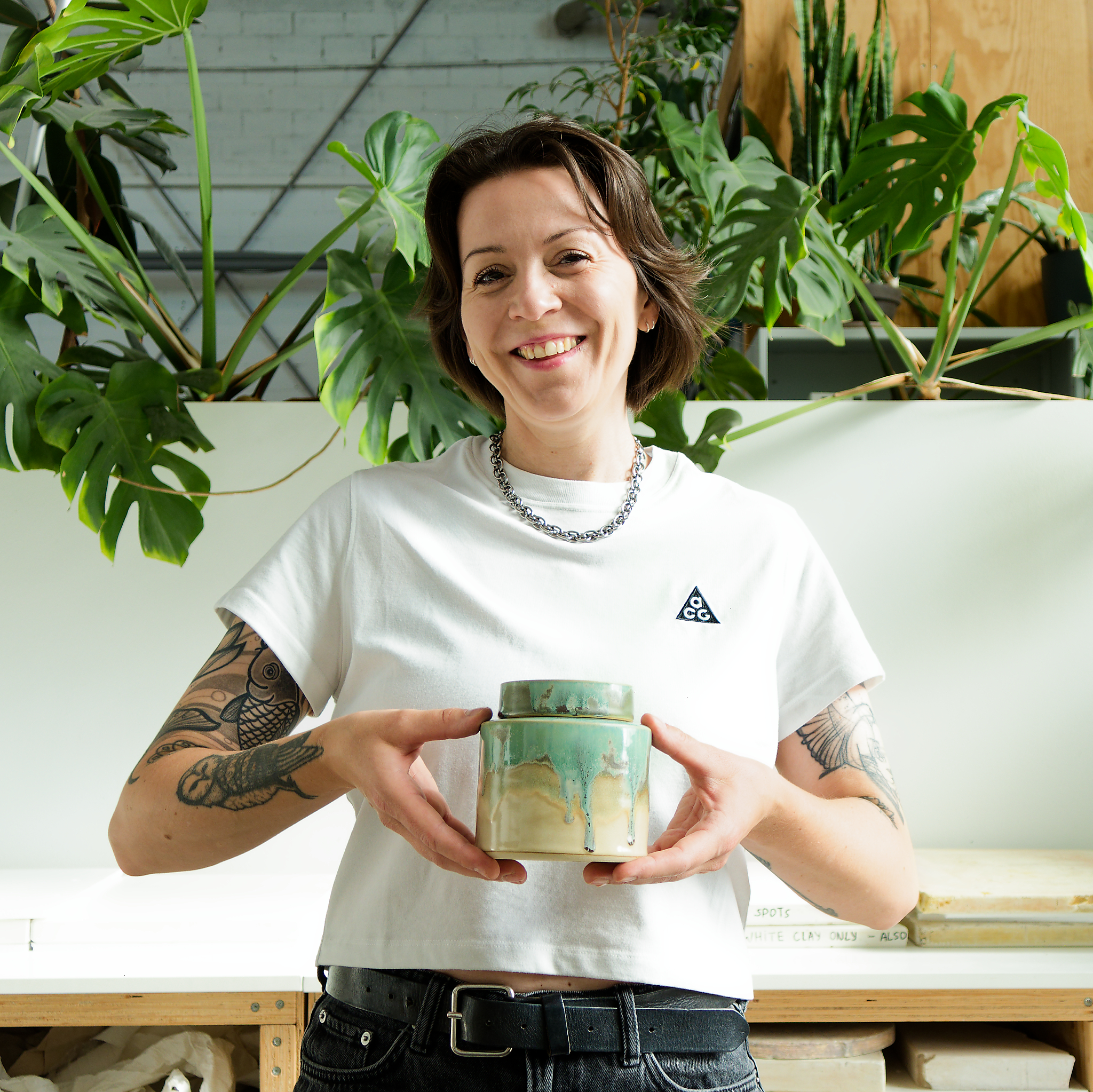 Cathy Daniels holding a lidded ceramic jar in her plant-filled Berlin studio.